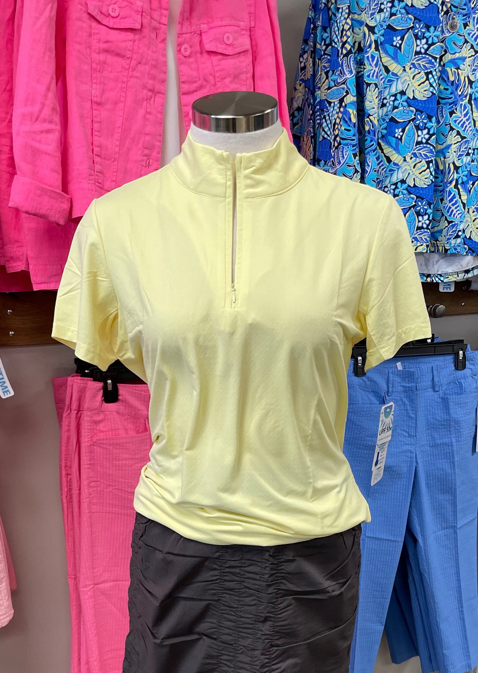 Mannequin wearing a yellow top and brown skirt in a store setting with colorful clothing in the background.