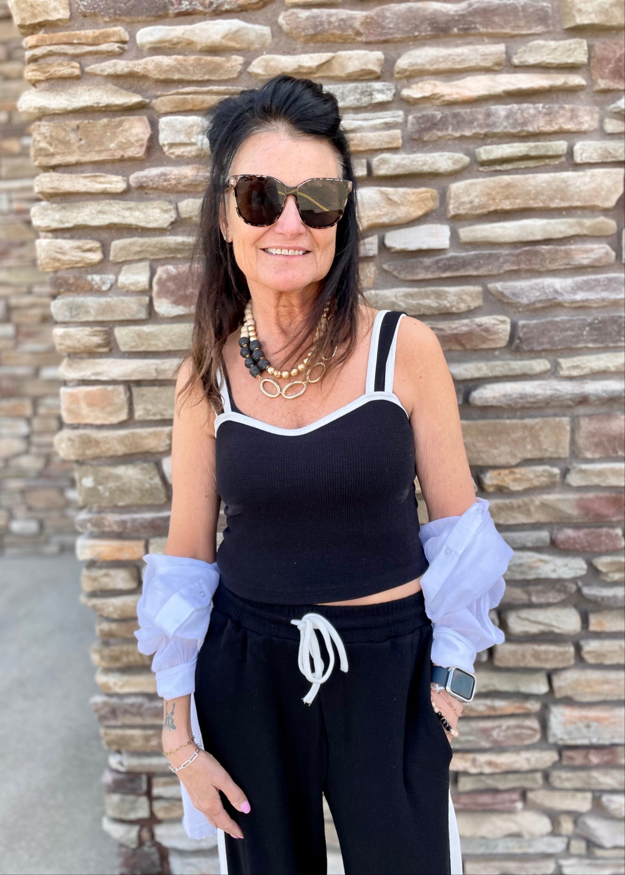 Woman wearing sunglasses and a black top with a stone wall background