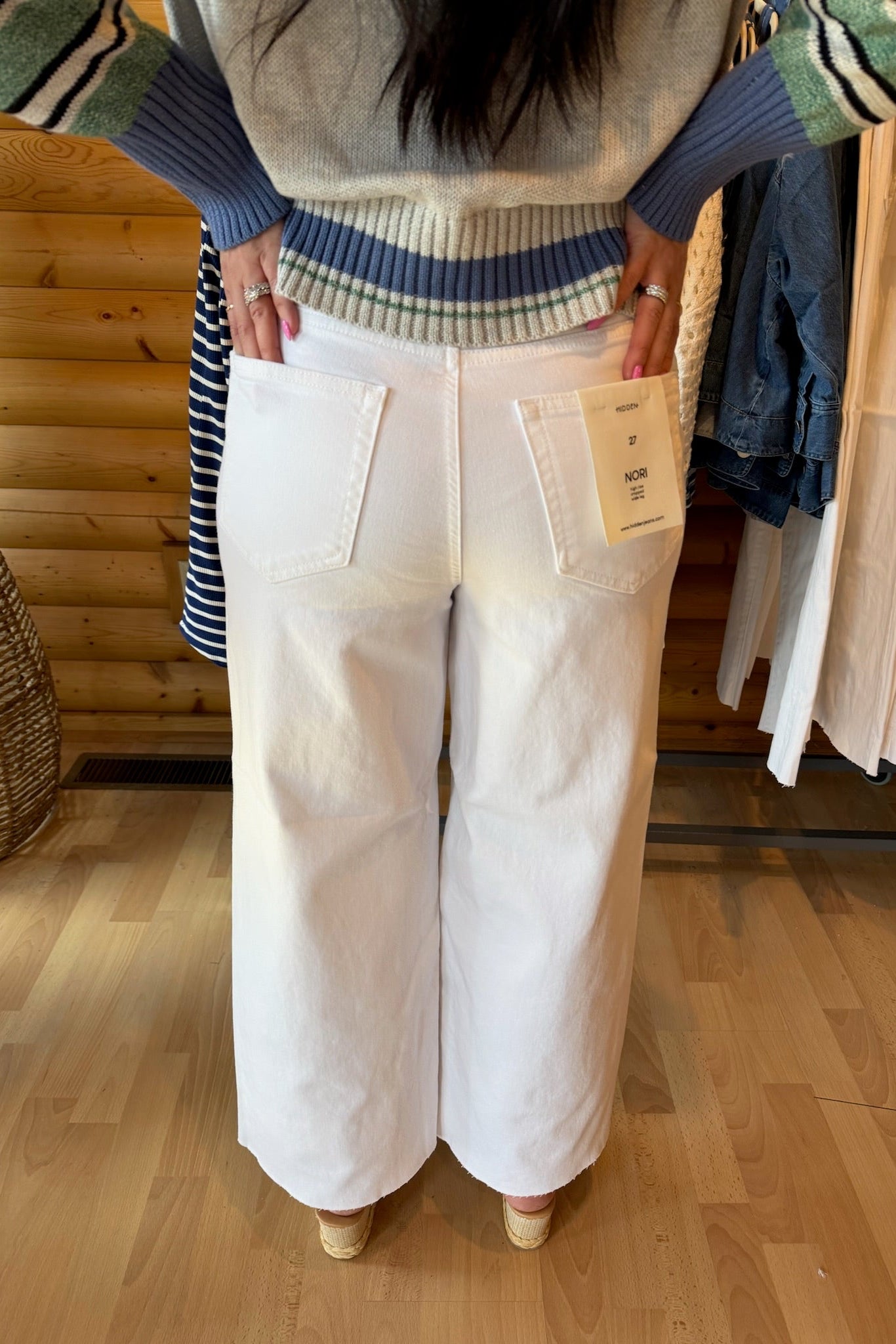 Person wearing white pants with a clothing tag, standing in a store with wooden flooring and wooden panel walls.