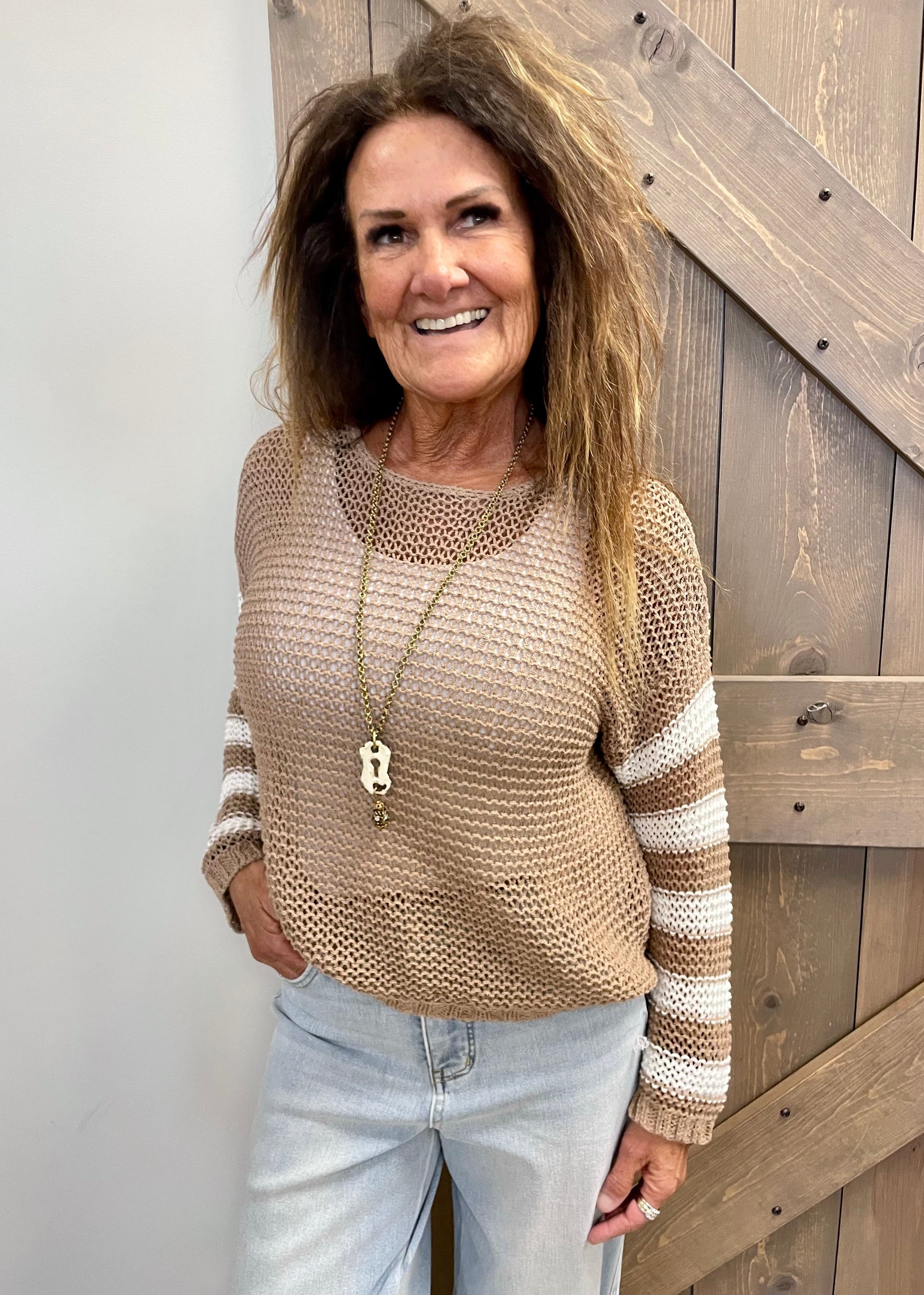 Woman wearing a beige and brown striped sweater standing in front of a wooden door.