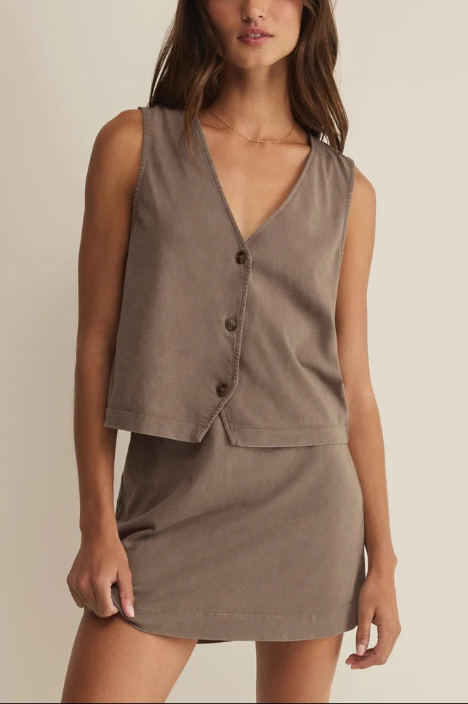 Woman wearing a brown vest and skirt set against a plain background