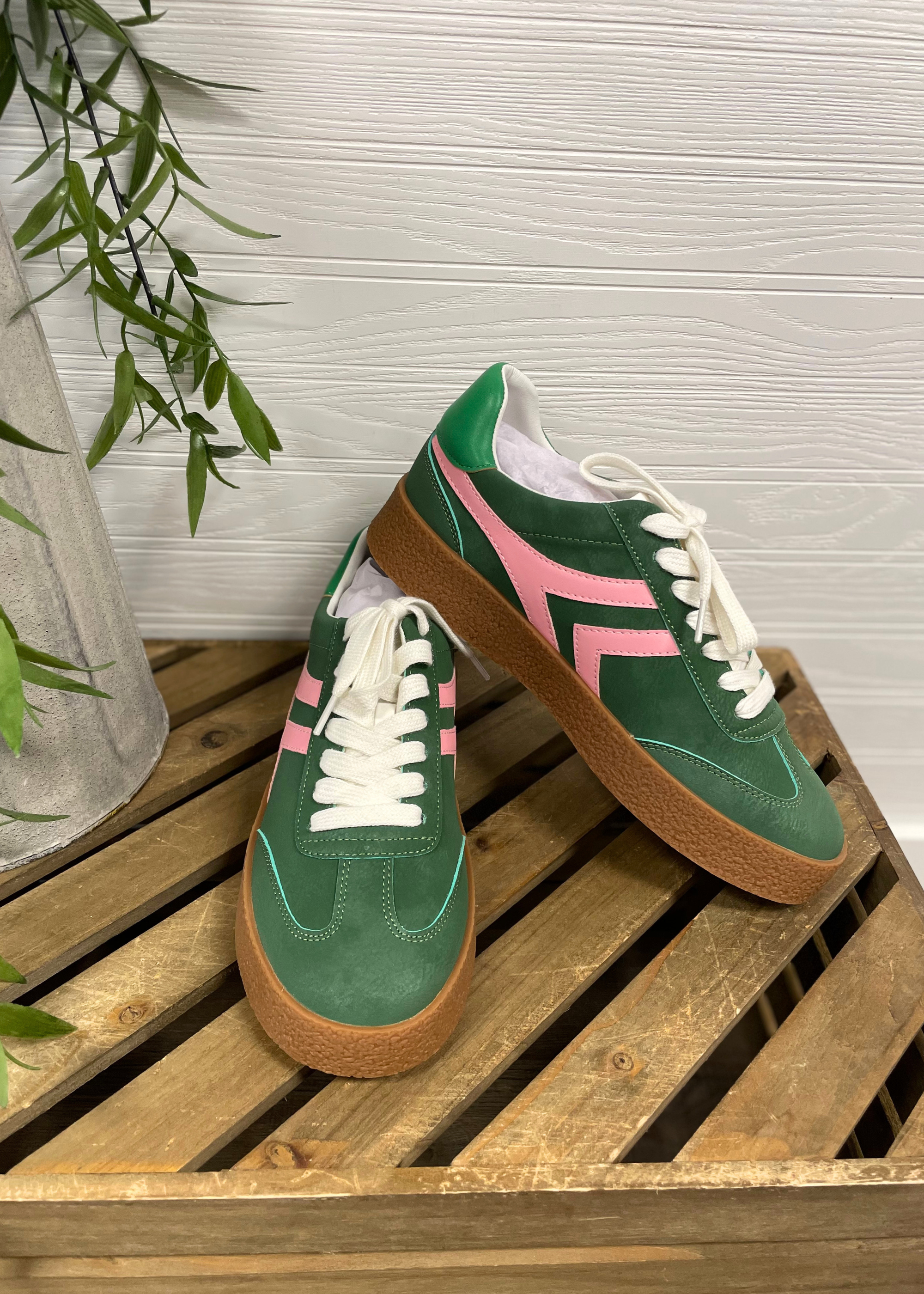 Green and pink sneakers with brown soles on a wooden surface.