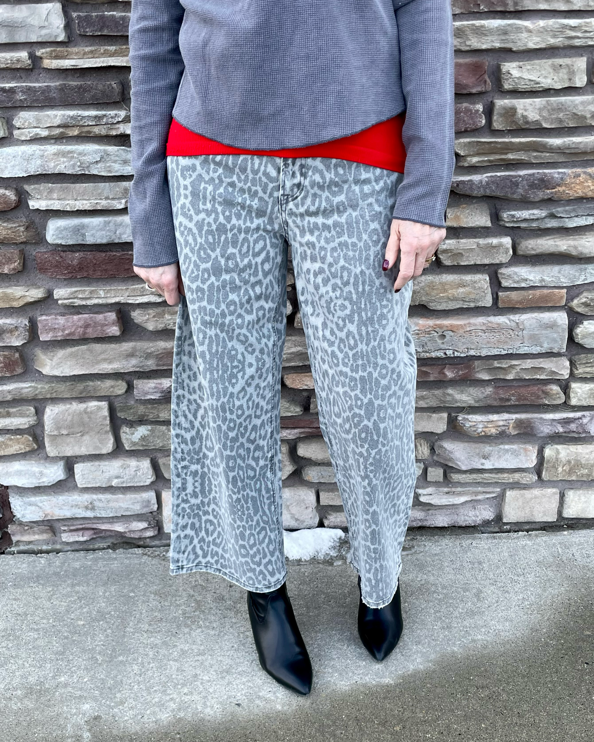 Person wearing gray leopard print pants and a red and charcoal shirt against a stone wall.
